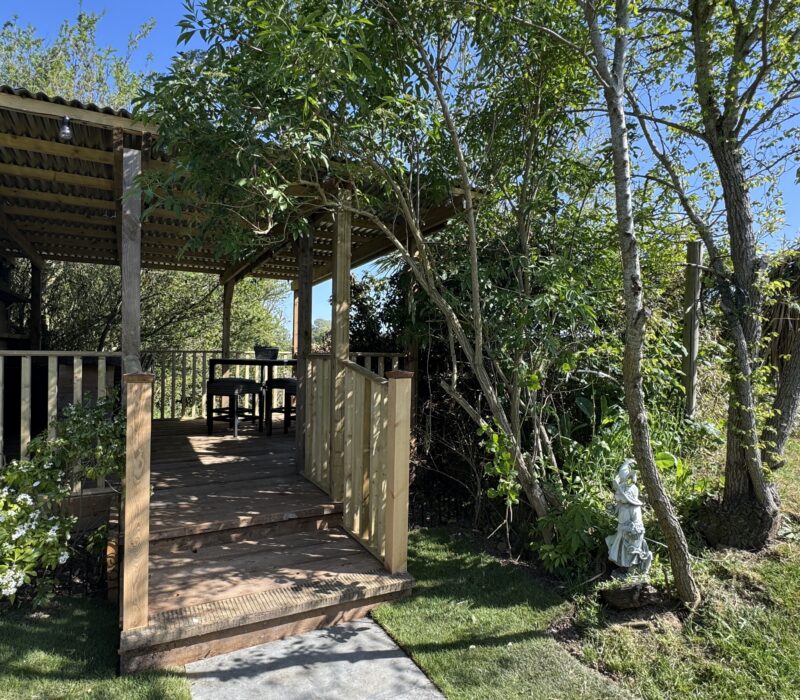The entrance of the barn area is framed with a willowy tree, You can just see inside the hand rails to the timber floor and table and chairs.